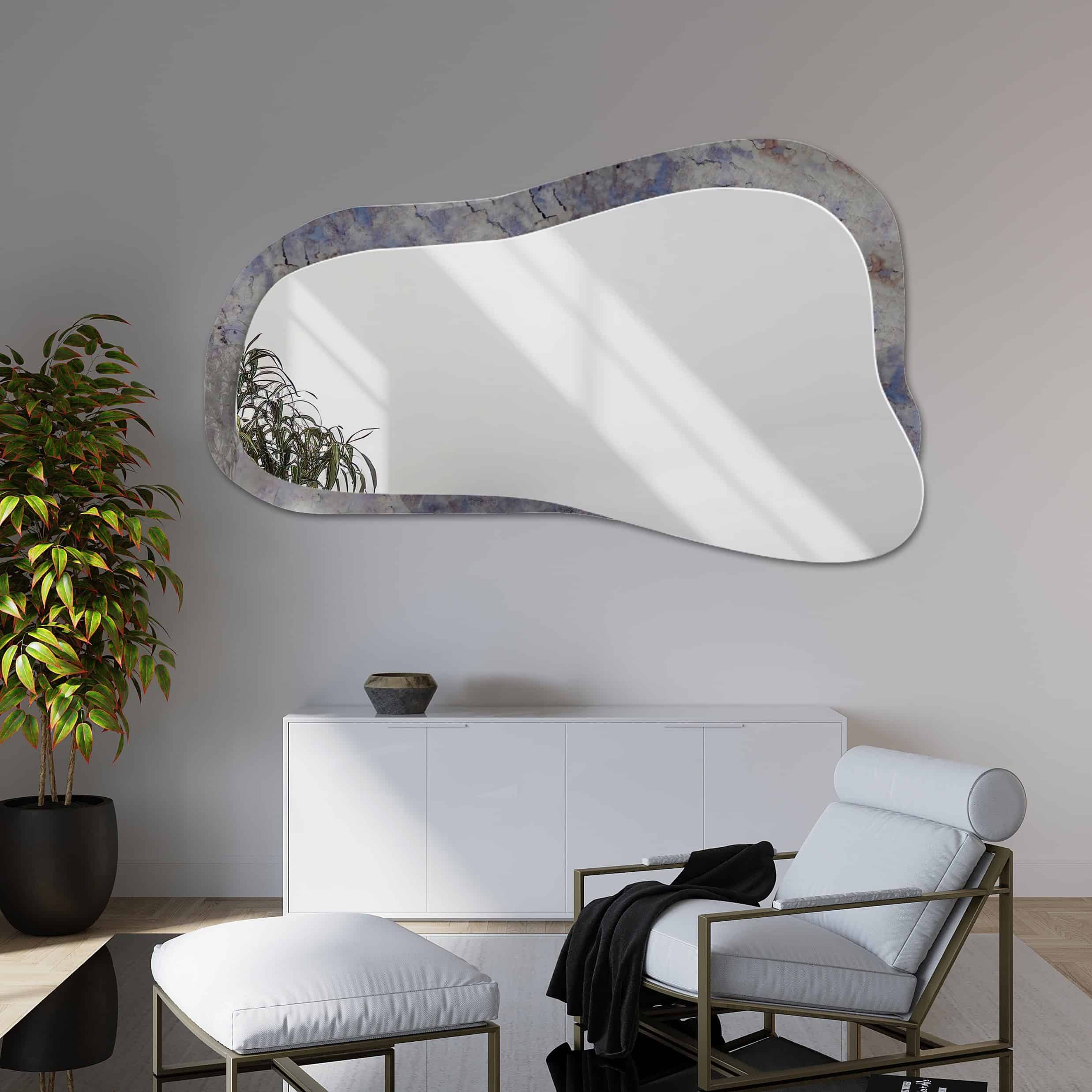 Wandspiegel met organische vorm en marmerlook rand in grijs- en blauwtinten, gemonteerd in een modern interieur met witte meubels en een elegante fauteuil.